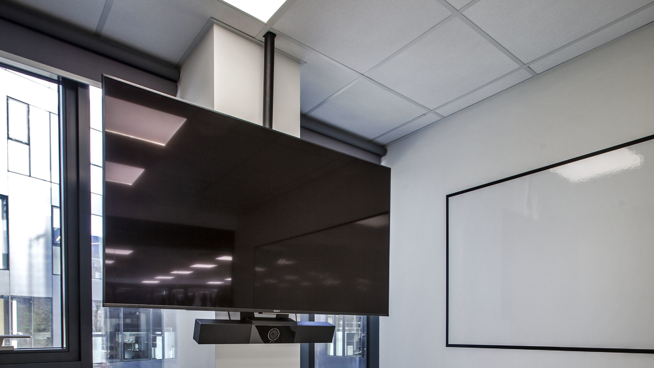 Mała sala spotkań Assa Abloy ze stołem, krzesłami, białą tablicą i dużym monitorem z kamerą na stojaku – realizacja PROAV