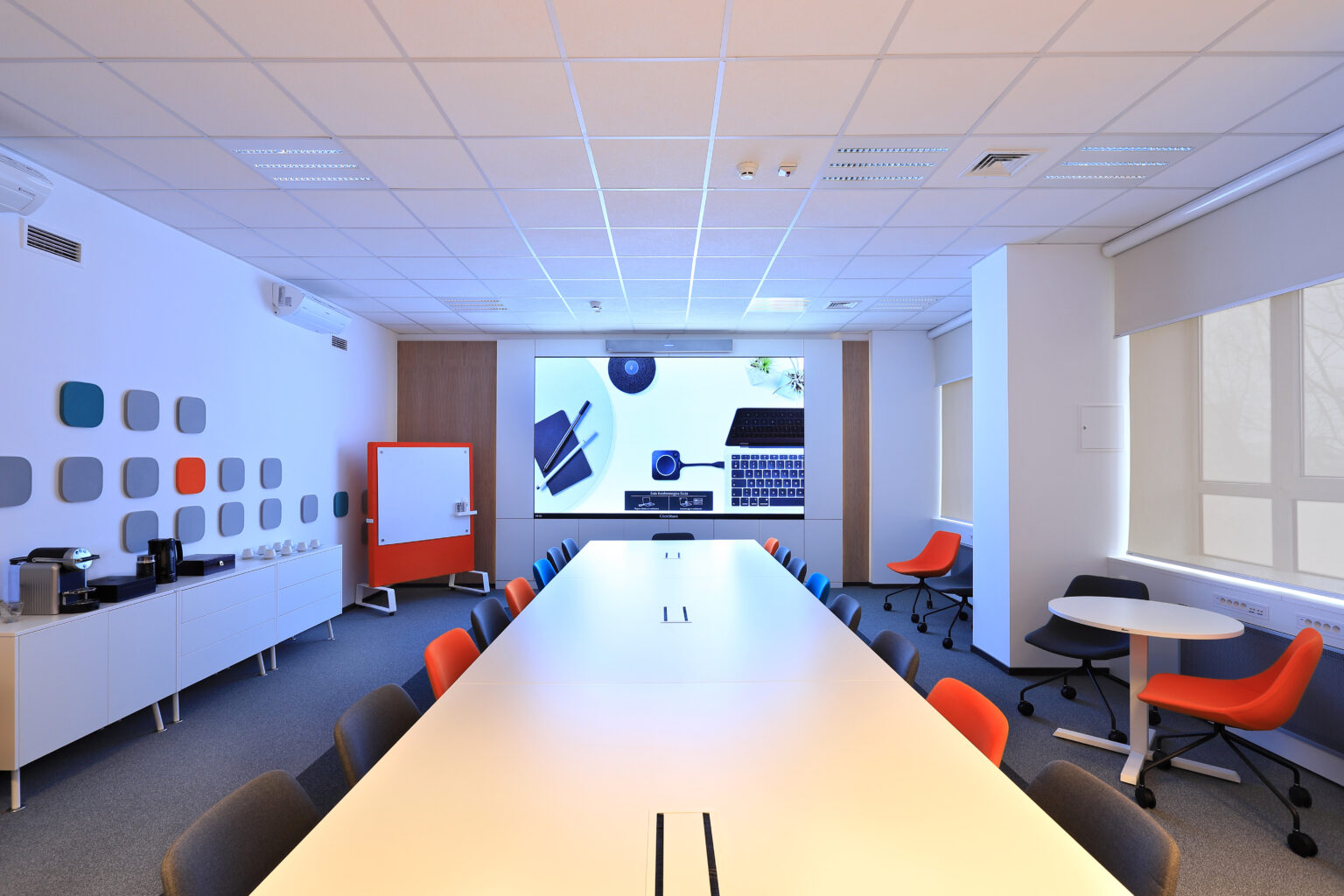 Duża sala spotkań Siemens z długim stołem, ekranem LED w zabudowie i kolorowymi krzesłami