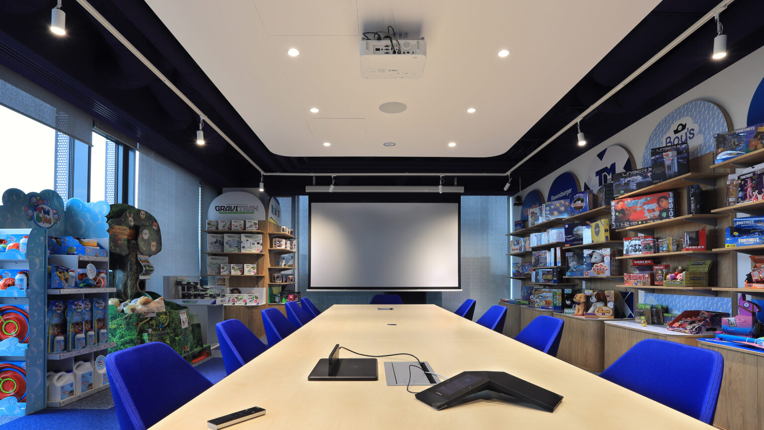 Sala konferencyjna TM Toys z projektorem na suficie, ekranem i długim stołem