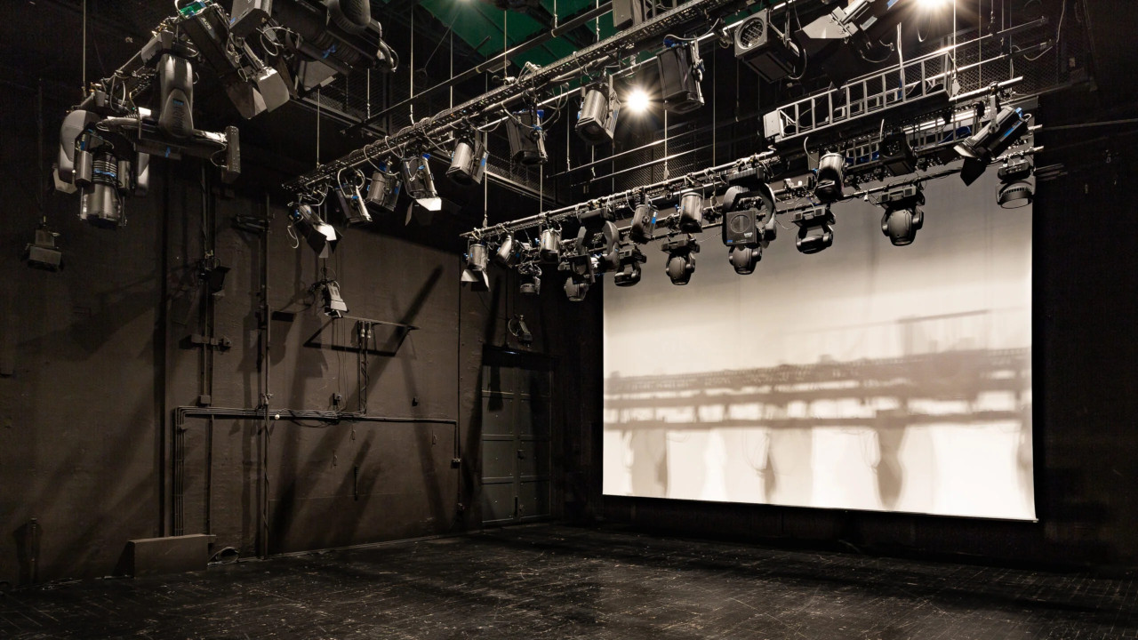 Scena teatralna z rozwiniętym dużym białym ekranem projekcyjnym i rzędami reflektorów na kratownicach nad sceną