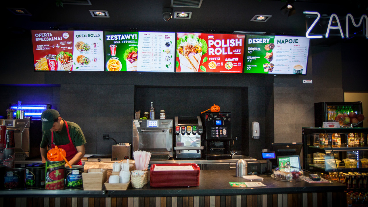 Cztery ekrany menu nad ladą lokalu gastronomicznego z ofertą, cenami i zdjęciami potraw