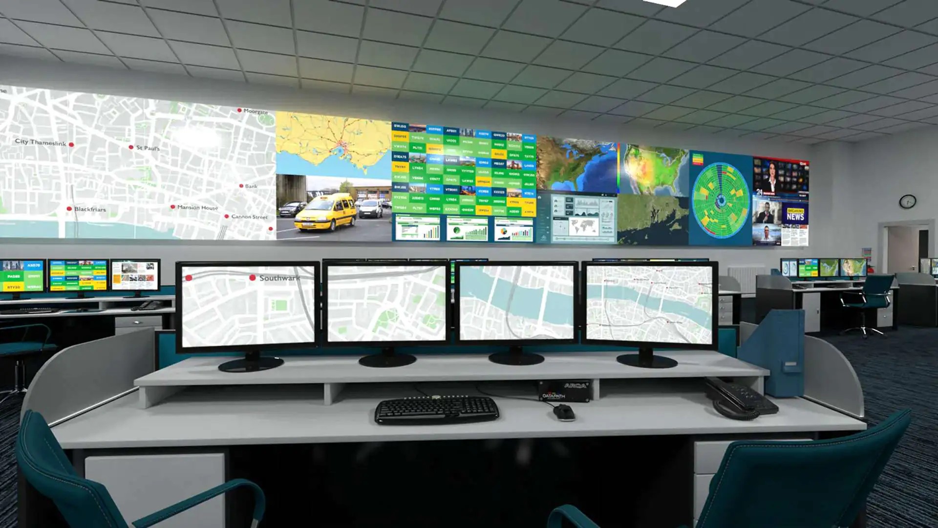 Stanowisko operatora z czterema monitorami i przełącznikiem KVM Datapath Arqa przed długą, jednolitą ścianą wizyjną LED z mapami i danymi